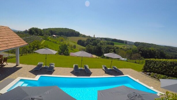 A swimming pool with lounge chairs and umbrellas, surrounded by a landscaped garden and a view of rolling hills. - Apartment Adlerhorst - Schwalbenhof Farm (Sankt Stefan im Rosental)