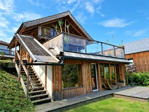 A wooden house with a balcony, a staircase, and a large window.