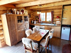 A wooden cabin interior with a dining table, chairs, a kitchen area, and a refrigerator.