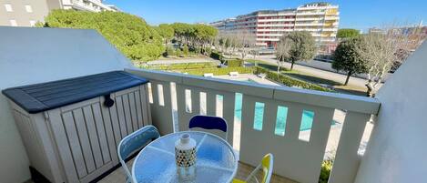 A balcony with a table and chairs, a small heater, and a view of buildings and trees.