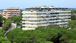 Un hotel de varios pisos con balcones, zona de estacionamiento y zonas verdes circundantes.