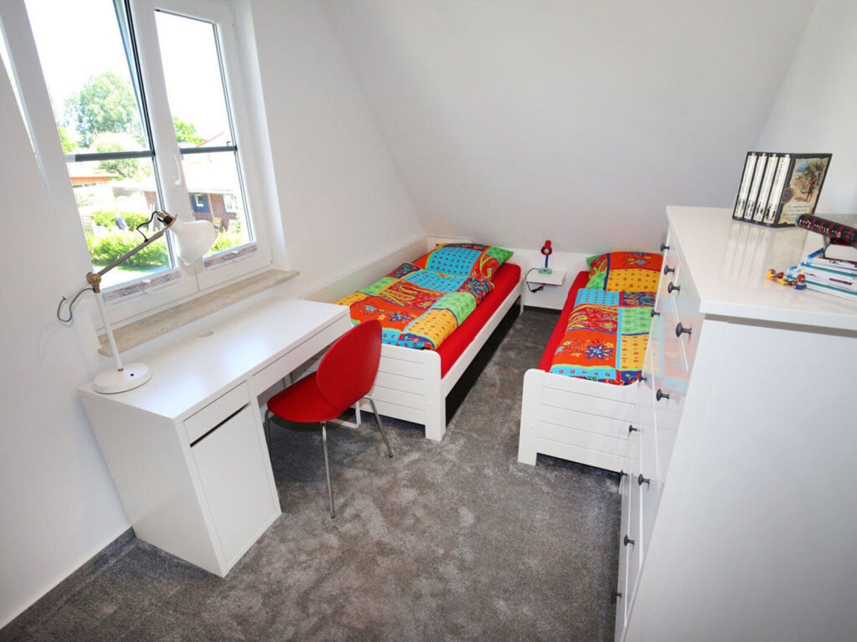 A bedroom with two single beds, a desk, a chair, and a window.