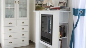 A room with a white cabinet with glass doors, a small bookshelf with books and a framed picture, and a window with a curtain. - Droom Unter Reet 2 Comfortable Holiday Residence (Rerik)