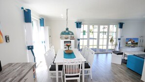 A bright kitchen with white cabinets, a dining table with chairs, and a TV. - Droom Unter Reet 2 Comfortable Holiday Residence (Rerik)