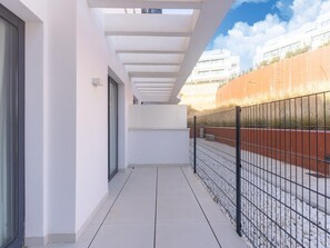 A covered balcony with a tiled floor, a metal fence, and a building in the background.