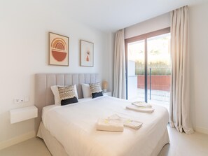 A modern hotel room with a large bed, two pillows, a nightstand, and a window with curtains.