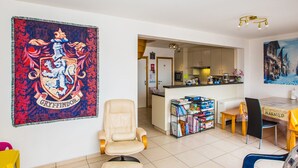 A living room with a large Gryffindor crest, a beige armchair, a dining table with chairs, and a bookshelf filled with books. - Duplex Apartment Near the Center (Middelkerke)