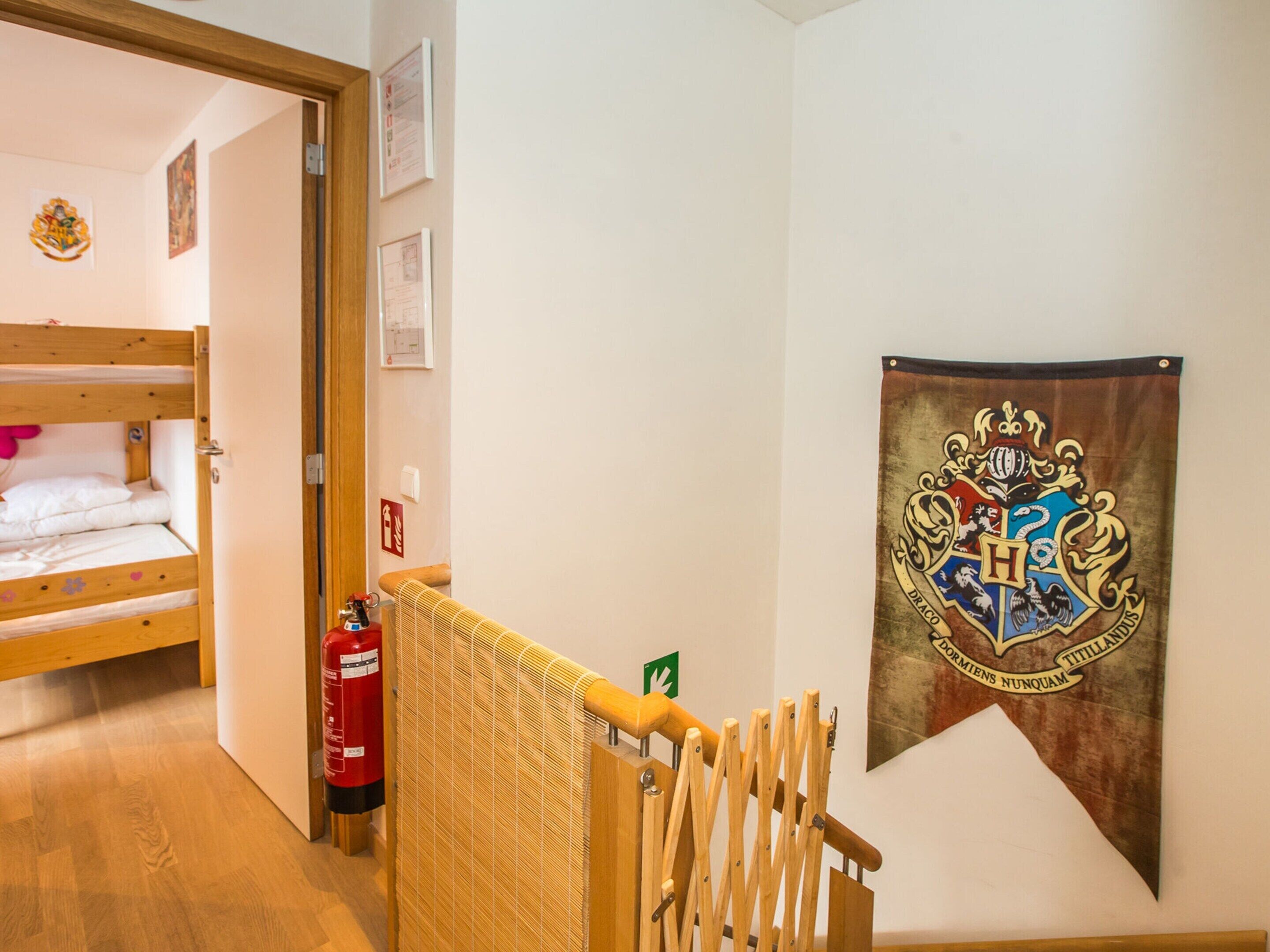 Une chambre avec un lit superposé, un extincteur, une rambarde en bois et une bannière ornée d’un blason.