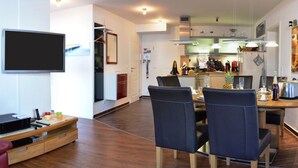 A modern living room with a flat-screen TV, a wooden entertainment unit, and a dining area with a table and chairs. - Siam Comfortable Holiday Residence (Borkum)