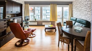 Een moderne woonkamer met een eetgedeelte, een bank, een televisie en een stadszicht door grote ramen.