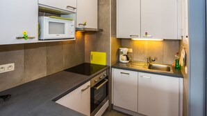 Een kleine keuken met witte kastjes, een magnetron, een koffiezetapparaat en een spoelbak.