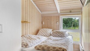 Une chambre à coucher avec un lit, des murs en bois, une fenêtre et une vue sur la verdure à l’extérieur.