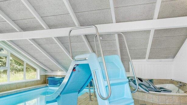 Une piscine intérieure avec un toboggan, un jacuzzi et une fenêtre laissant entrer la lumière naturelle.