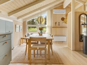 Un coin repas avec une table en bois, des chaises et un tapis. Une fenêtre offre une vue sur la verdure à l’extérieur.