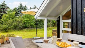 An outdoor wooden deck with a table set for dining, surrounded by potted plants and a view of a lush garden. - 7 Person Holiday Home in Jerup (Jerup)