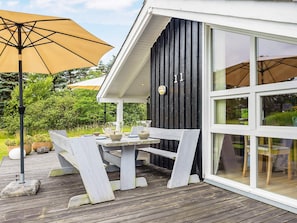A wooden deck with a table and chairs, a large umbrella, and a building with a black exterior and white trim. - 7 Person Holiday Home in Jerup (Jerup)