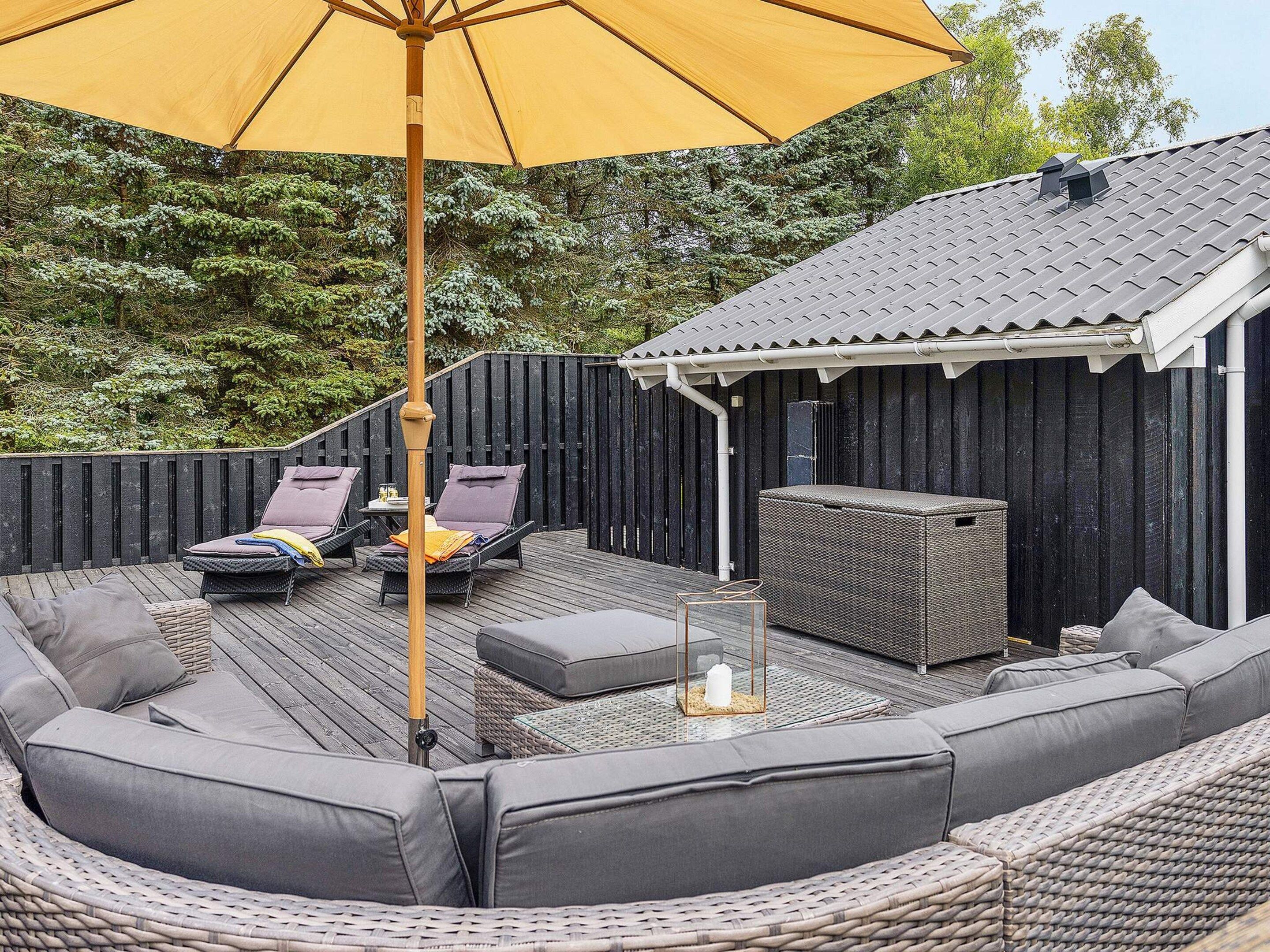Een terras buiten met rieten meubilair, een overdekte zithoek en een grote parasol.