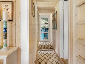 Un couloir en bois avec un tapis à motifs, une porte donnant sur un salon bleu et une bougie posée sur un chandelier.