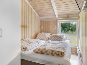 Une chambre à coucher avec un lit, des murs en bois, une fenêtre et une vue sur la verdure.