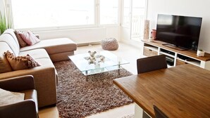 A modern living room with a sofa, ottoman, coffee table, and a TV on a wooden stand. - Apartment in Nieuwpoort by the Beach (Nieuwpoort)