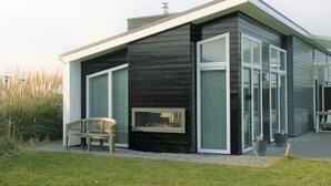 A modern house with a black exterior, large windows, and a bench in the front yard. - Chalet in Zeeland by the Lake (Wemeldinge)
