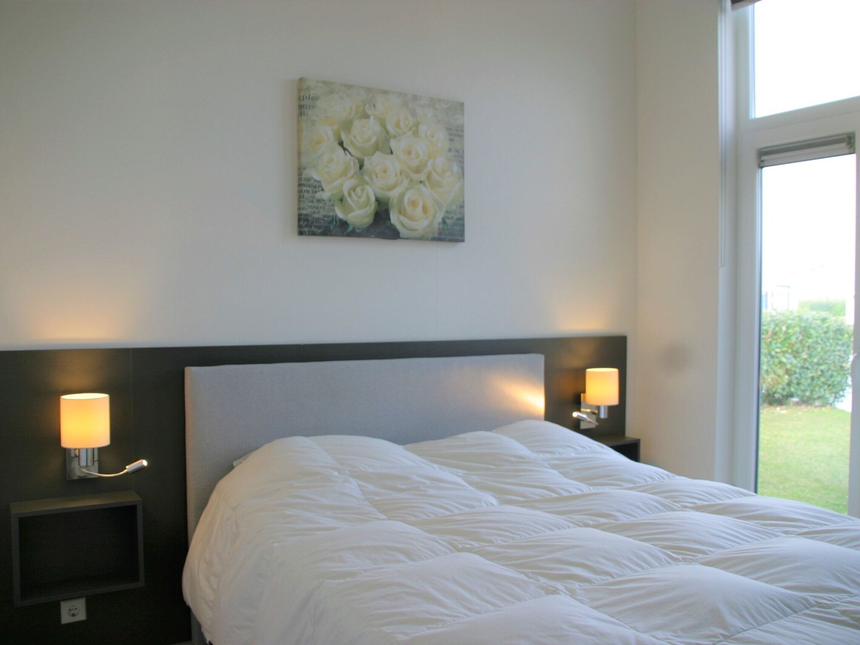 A hotel room with a large bed, two bedside lamps, and a wall-mounted painting of white roses.