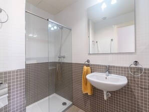 Ein Badezimmer mit einer Duschkabine aus Glas, einem weißen Waschbecken und einem Spiegel darüber.