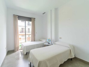 Ein kleiner, sauberer Raum mit zwei Betten, einem Fenster mit Vorhängen, einem kleinen Tisch mit Globus und Blick auf ein Gebäude.