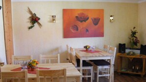 A dining area with a wooden table and chairs, a painting on the wall, and a small side table with a vase of flowers. - Fantastic Apartment in Reinhardshagen (Reinhardshagen)