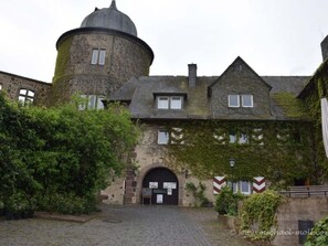 Un bâtiment historique doté d’une tour ronde, de murs en pierre et de fenêtres recouvertes de lierre.
