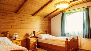 Ein Schlafzimmer einer Holzhütte mit zwei Betten, einem Nachttisch, einer Lampe und einem Fenster mit Vorhängen.
