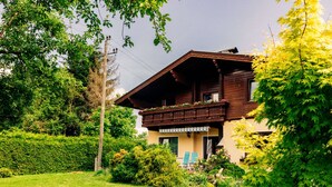 Ein traditionelles Chalet mit Holzbalkon, umgeben von üppiger Vegetation und einem gepflegten Garten.