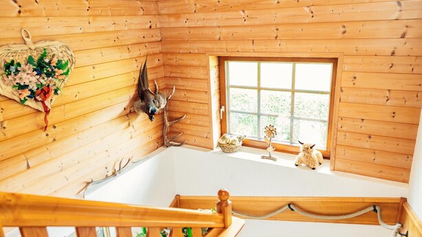 Ein Holzhütten-Interieur mit einer Holztreppe, einem Fenster mit Blick auf Grünflächen und an der Wand befestigten Hirschgeweihen.