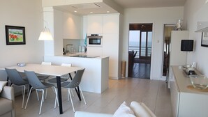 A modern kitchen with white cabinetry, a central island, and a dining area with a table and chairs. - Apartment in Nieuwpoort Near the Beach (Nieuwpoort)