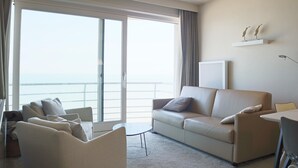 A modern living room with a sofa, armchairs, and a coffee table. There is a large window with a view of the sea. - Apartment in Nieuwpoort Near the Beach (Nieuwpoort)