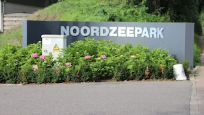 Un cartel de Noordzeepark con una señal de advertencia y flores al frente.