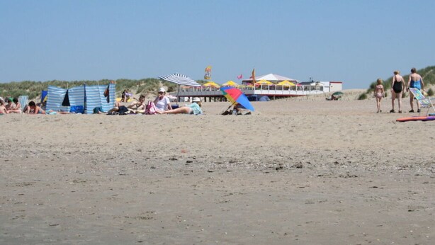Una playa con tiendas de campaña, un muelle y un edificio con una bandera.