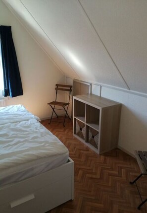 Quarto com cama, uma cadeira de madeira e uma estante branca.