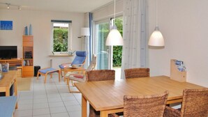 Una sala moderna con una mesa de comedor de madera, sillas de mimbre, un televisor y un ventanal con cortinas.