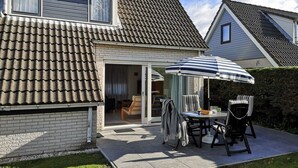 Una casa con techo de tejas, un patio con mesa y sillas, y un espacio al aire libre cubierto.