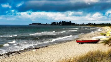 A beach with a row of boats on the sand and a distant shoreline with buildings.