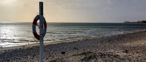 Un flotador sujeto a un poste en una playa pedregosa, con el océano al fondo.