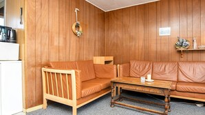 A cozy living room with a wooden panel wall, a brown leather sofa, a wooden coffee table, and a small wooden cabinet. - 3 Person Holiday Home in Sydals (Sydals)