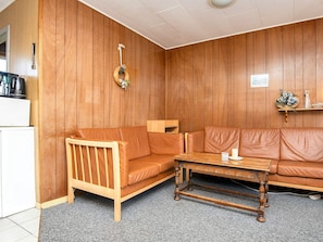 Un salon chaleureux avec un mur lambrissé, un canapé en cuir marron, une table basse en bois et un petit meuble en bois.
