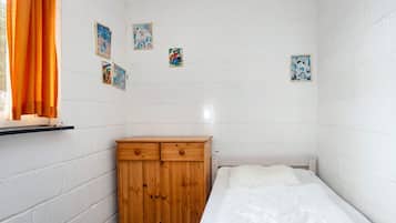 Quarto pequeno com uma cama de solteiro, paredes brancas, um guarda-roupa de madeira e uma janela com cortinas laranja.