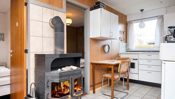 Una cocina compacta con estufa de leña, una mesa de comedor con sillas y un ventanal.