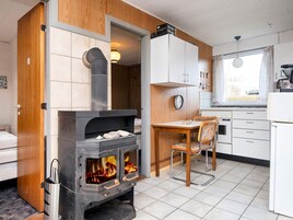 Una cocina compacta con estufa de leña, una mesa de comedor con sillas y un ventanal.