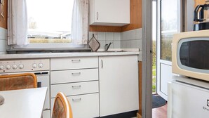 A compact kitchen with a stove, sink, and a microwave. There is a window with curtains and a view of the outside. - 3 Person Holiday Home in Sydals (Sydals)