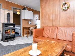A cozy living room with a leather sofa, a wooden table with a candle, and a wood-burning stove. - 3 Person Holiday Home in Sydals (Sydals)
