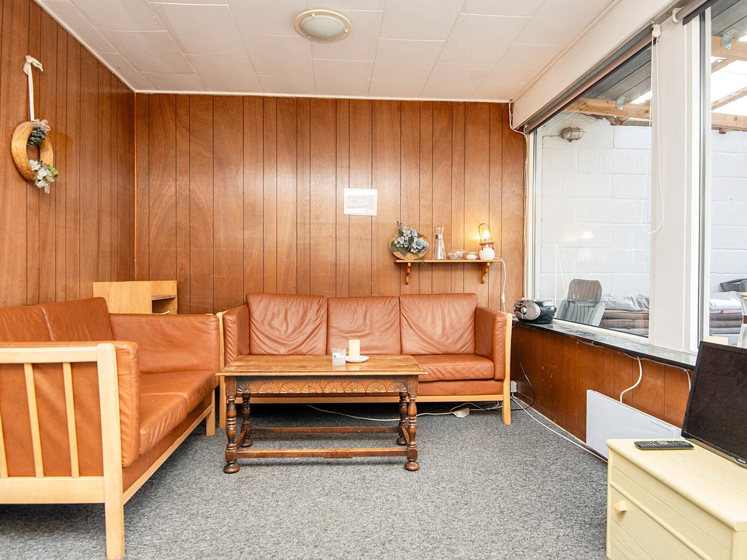 Ein Zimmer mit einer Holzwand, einem braunen Ledersofa, einem Holztisch und einem kleinen Schreibtisch mit einem Computer.